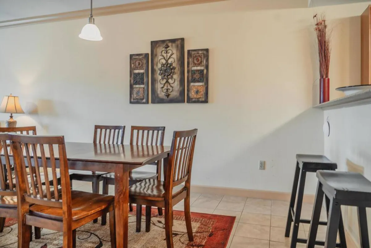 This warm, inviting interior scene highlights a dining table set beneath decorative wall art, complemented by a table lamp. The space is arranged for casual gatherings, dinners, and social moments, suggesting a welcoming atmosphere for returning from a night out.