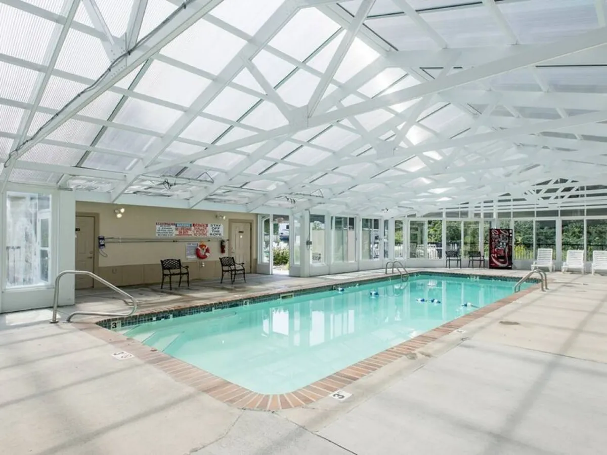 This image features an indoor swimming pool with large windows allowing plenty of natural light, comfortable seating along the poolside, and a tranquil, inviting atmosphere ideal for all ages year-round.