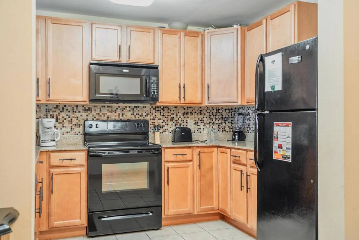 A modern kitchen with stainless steel appliances, granite countertops, wooden cabinetry, and a colorful backsplash. The setup is ideal for cooking, entertaining, and staying connected with guests in the adjacent living and dining spaces.