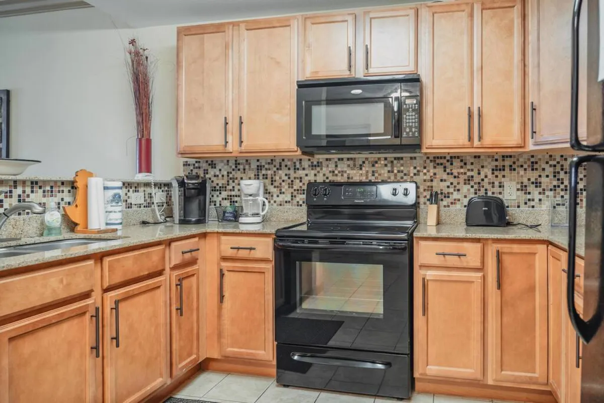 A spacious kitchen with black appliances, granite countertops, wooden cabinets, and a colorful backsplash, designed for cooking and entertaining. The inviting setting encourages culinary adventures and group meals before or after nights out.