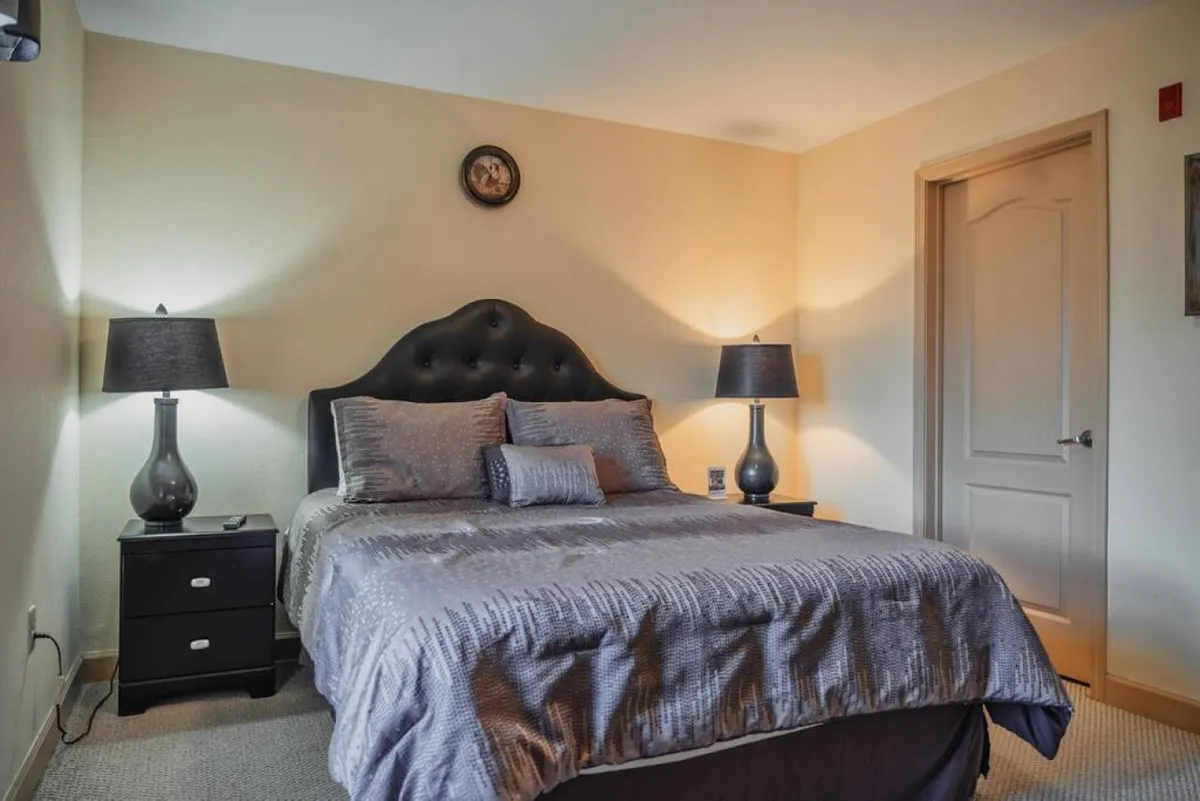 A calming bedroom scene featuring a bed with textured bedding, decorative lamps on either side, and tasteful wall art. The soft, natural light enhances the serene and inviting mood, suggesting a space designed for relaxation and restful sleep.