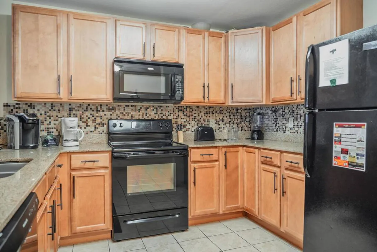 A spacious kitchen featuring stainless steel appliances, granite countertops, wooden cabinets, and a colorful backsplash. The space is set up for cooking and entertaining, evoking warmth and togetherness. The layout and finishings suggest both practicality for meal prep and an inviting setting for culinary gatherings.